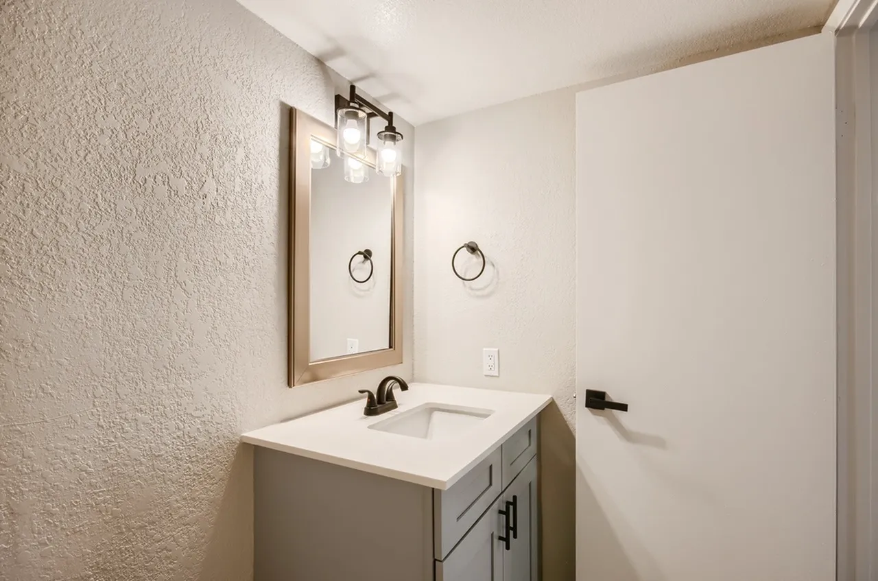 Bathroom, single vanity, wood-framed mirror, black faucet, white countertop, gray cabinet