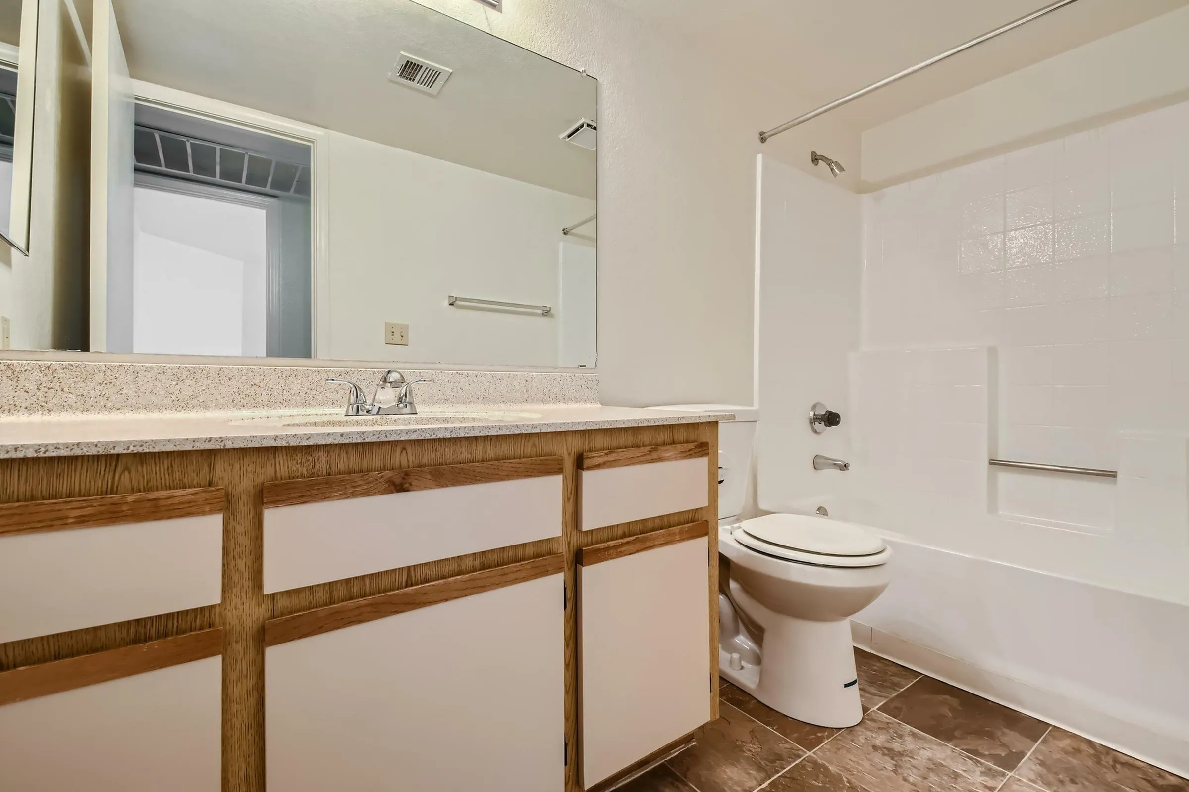 Bathroom, single vanity, speckled countertop, wood-tone cabinet trim, tub shower