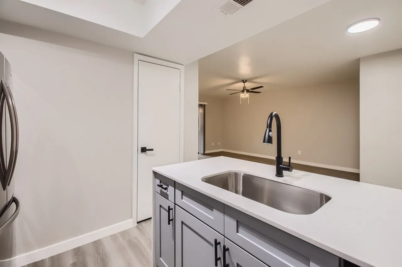 Undermount kitchen sink, black gooseneck faucet, white countertop, gray lower cabinets