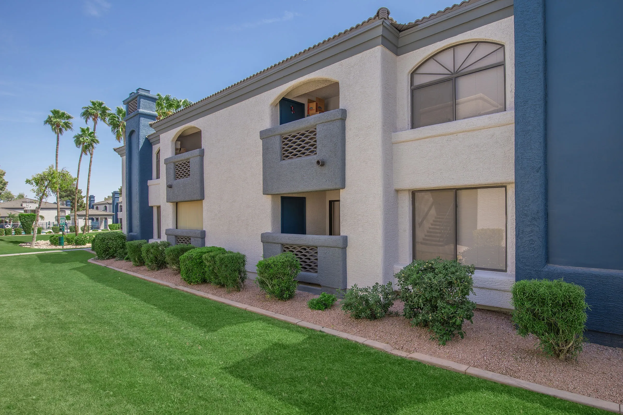 Two-story apartment building exterior, private balconies, landscaped lawn, shrubs
