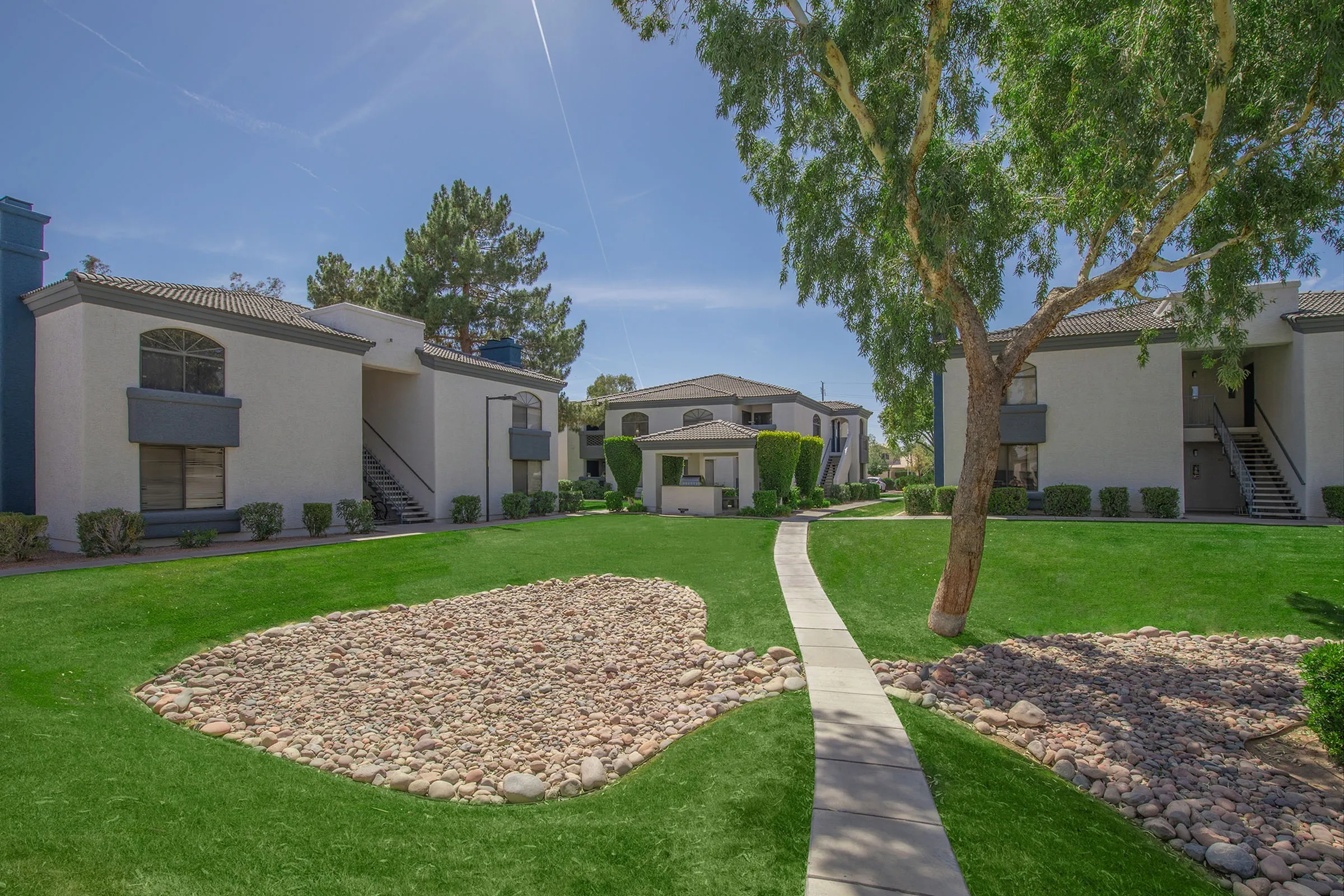 Courtyard walkway, green lawn, desert rock landscaping, mature trees, building exteriors