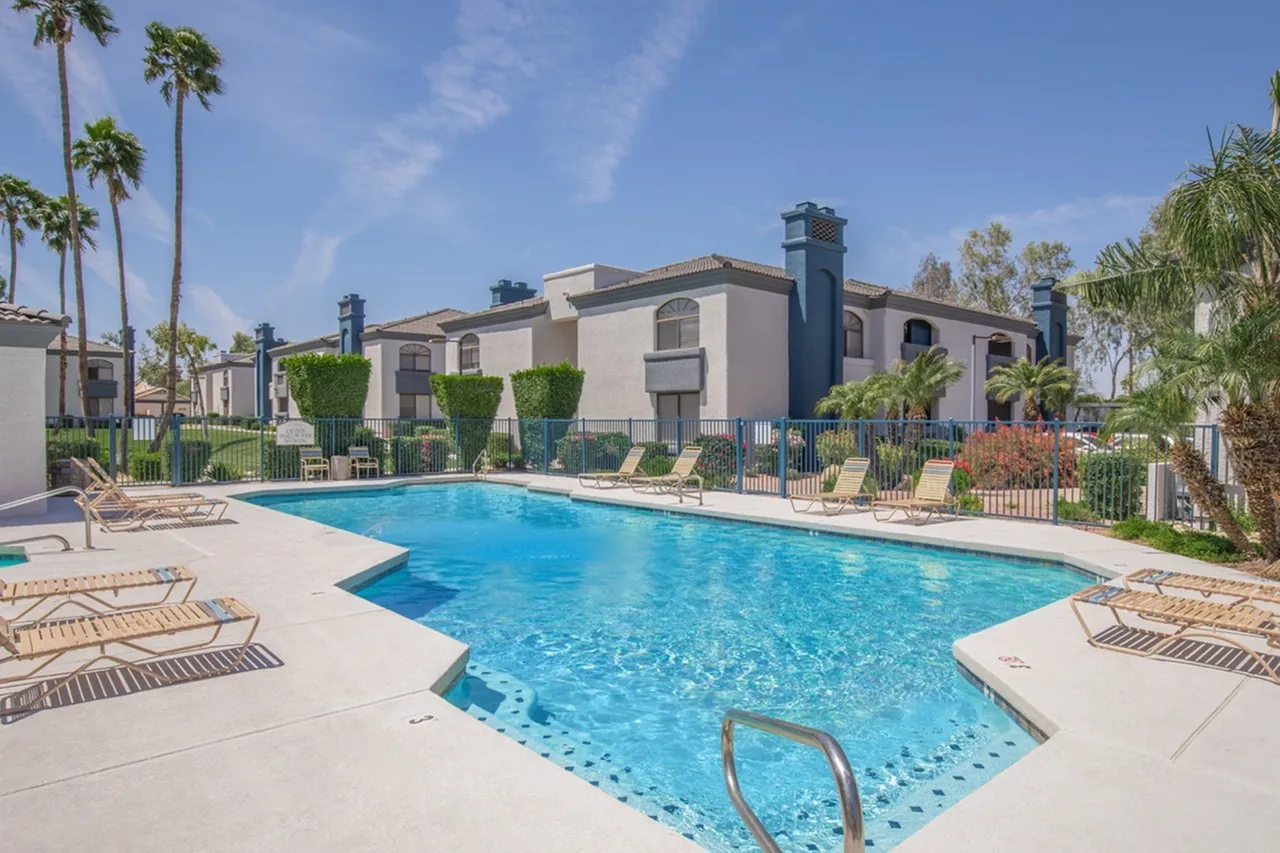 Community pool, lounge chairs, palm trees, two-story buildings