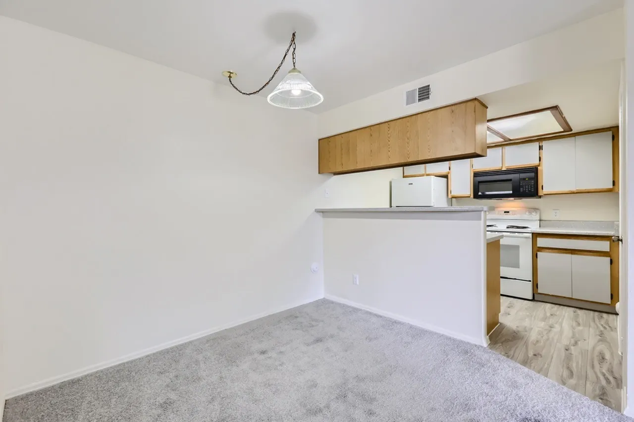 Kitchen peninsula, pendant light, wood-tone upper cabinets, white walls, carpet flooring