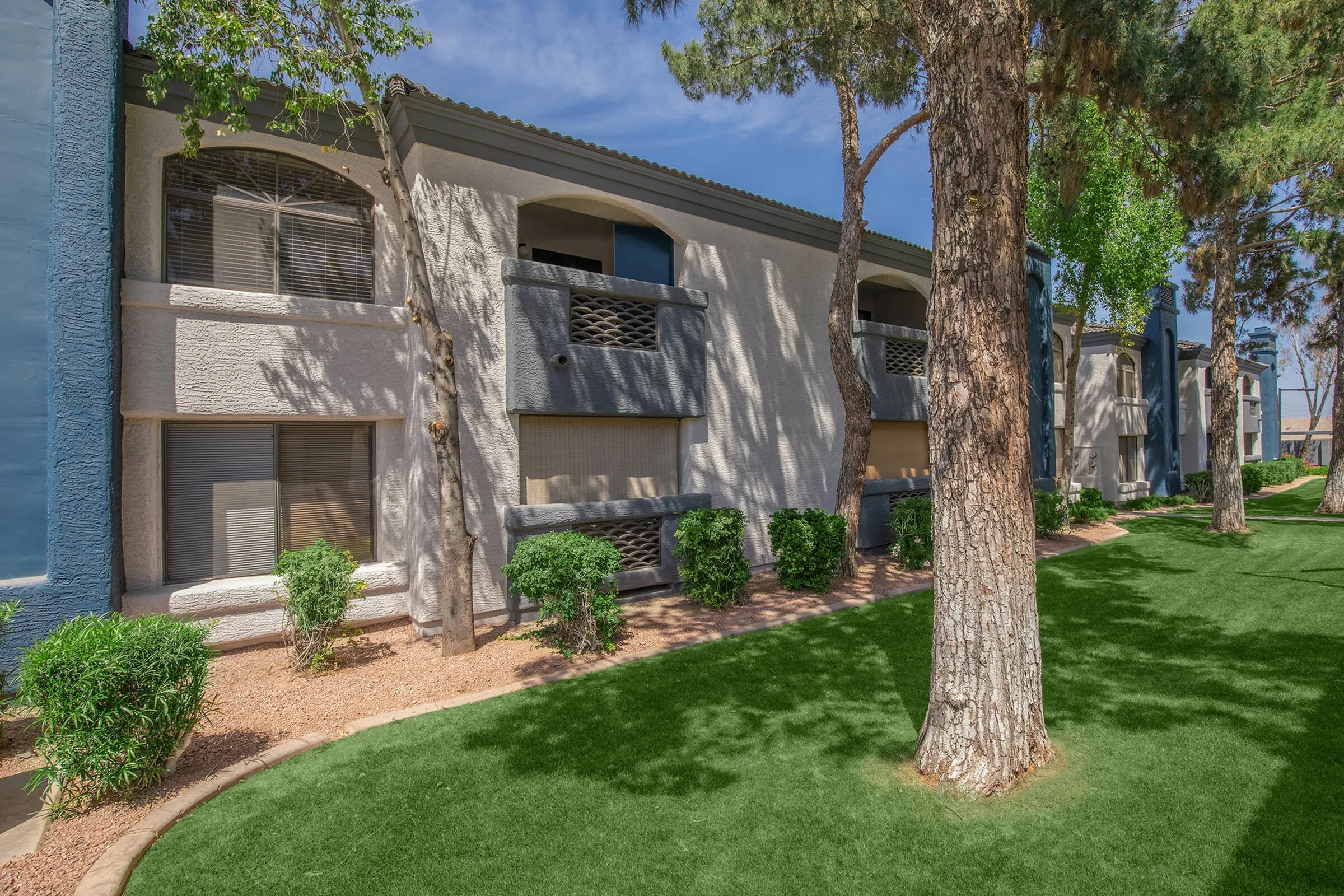Apartment building exterior, ground-floor patios, mature trees, landscaped lawn