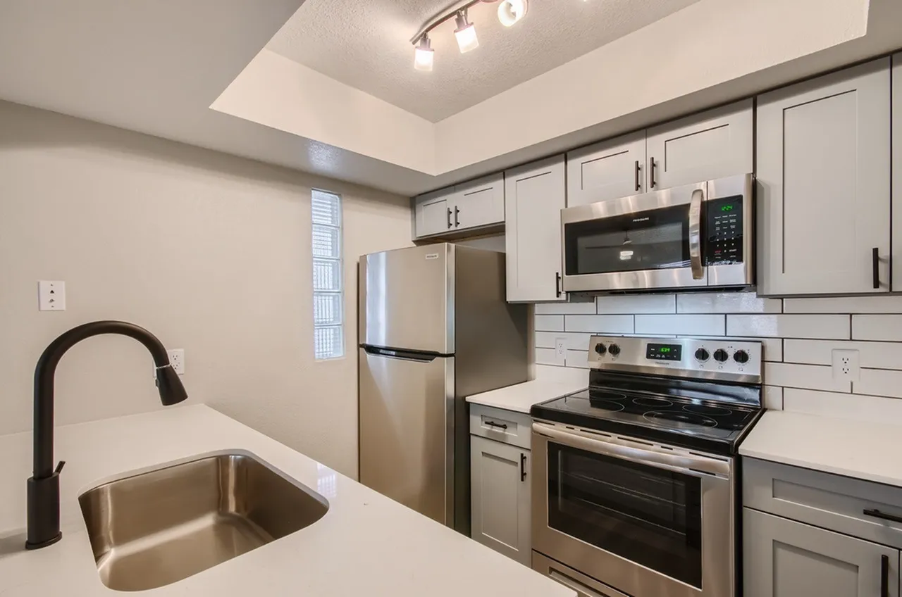 Stainless steel refrigerator, over-range microwave, electric range, subway tile backsplash, glass block window