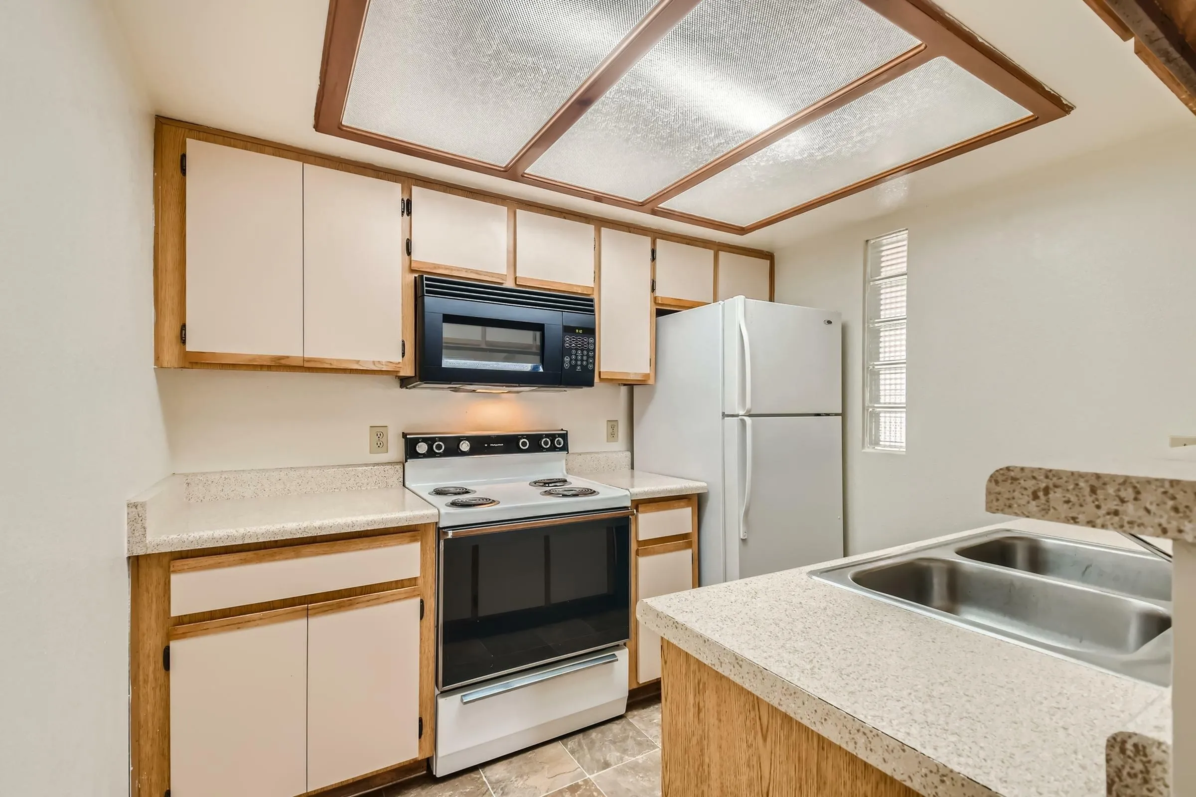 Kitchen, white refrigerator, over-range microwave, electric range, speckled countertop, wood-tone cabinet trim