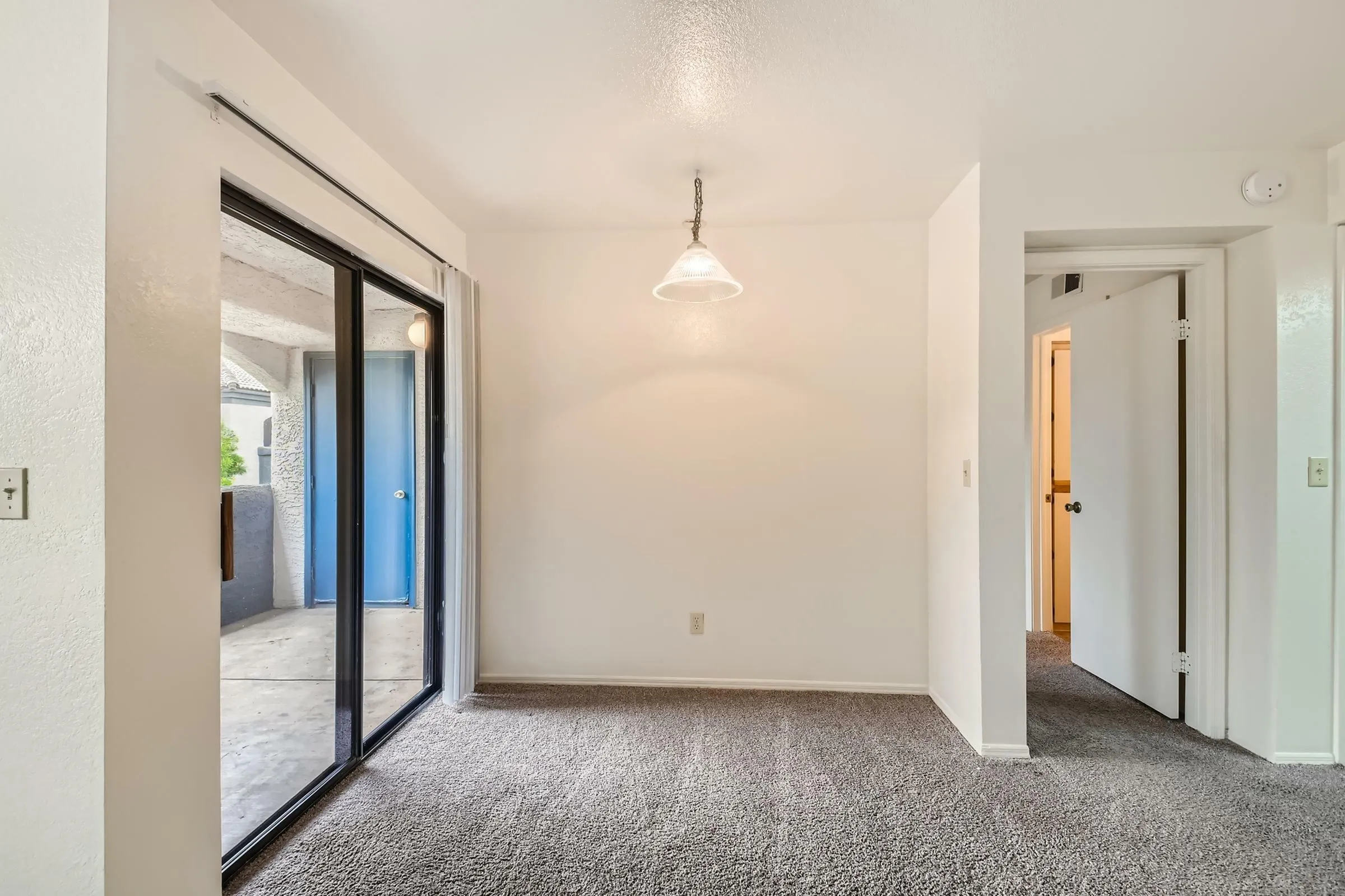 Dining area, pendant light, sliding glass door to patio, carpet flooring, doorway to hall