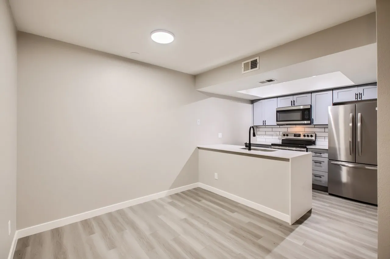 Kitchen peninsula with white countertop, stainless steel range and microwave, tile backsplash, light plank flooring