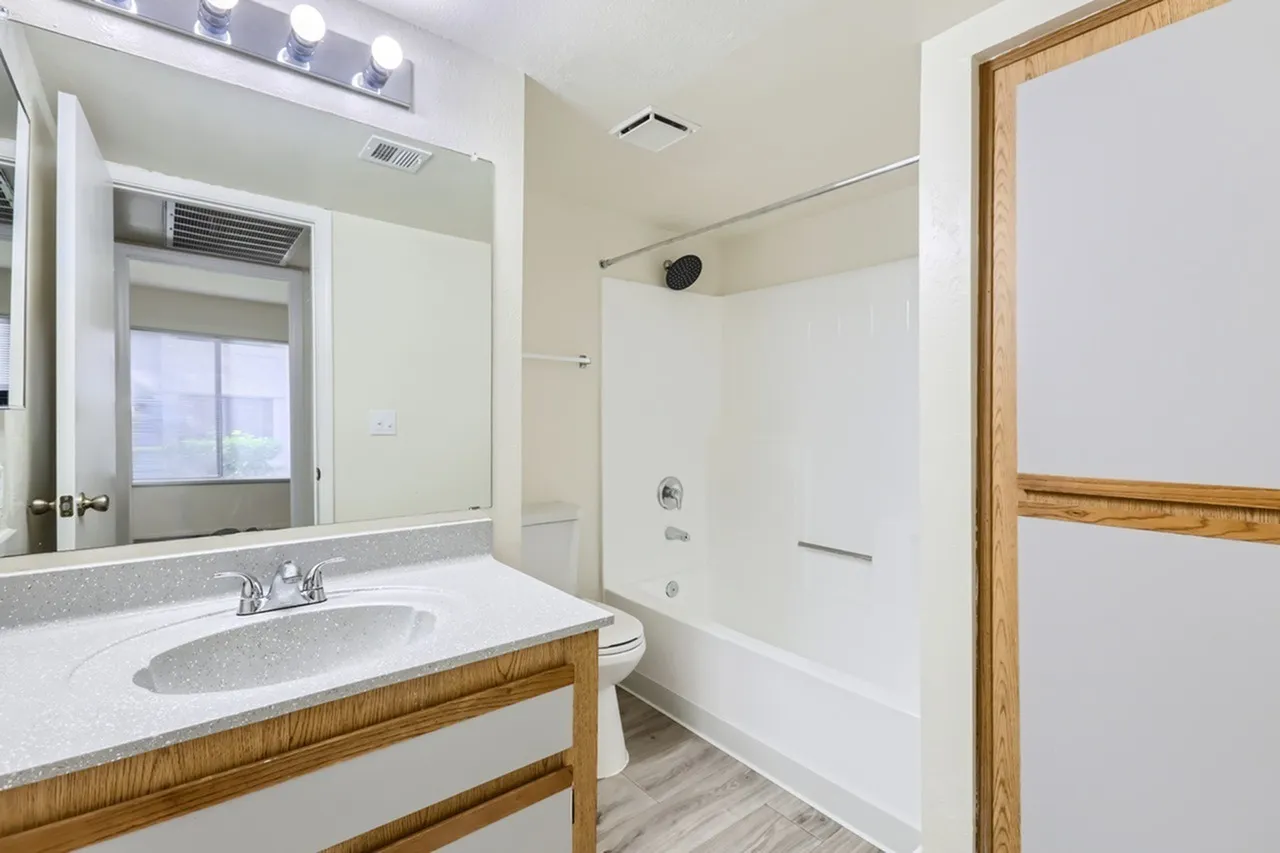 Bathroom, single vanity, speckled countertop, tub shower, wood-tone vanity trim