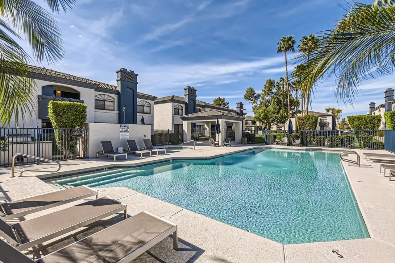 Resort-style pool, pool deck lounge chairs, covered ramada, palm trees, iron fence