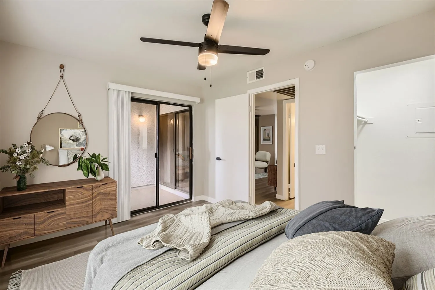 Primary bedroom, ceiling fan, sliding glass door with vertical blinds, walk-in closet, view into living area
