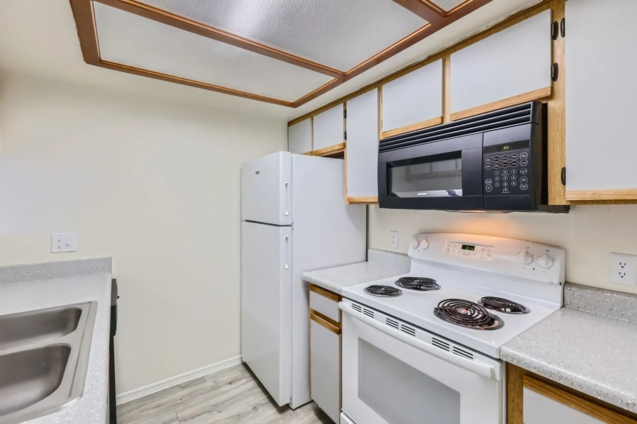 White refrigerator, over-range microwave, electric coil range, wood-tone cabinet trim