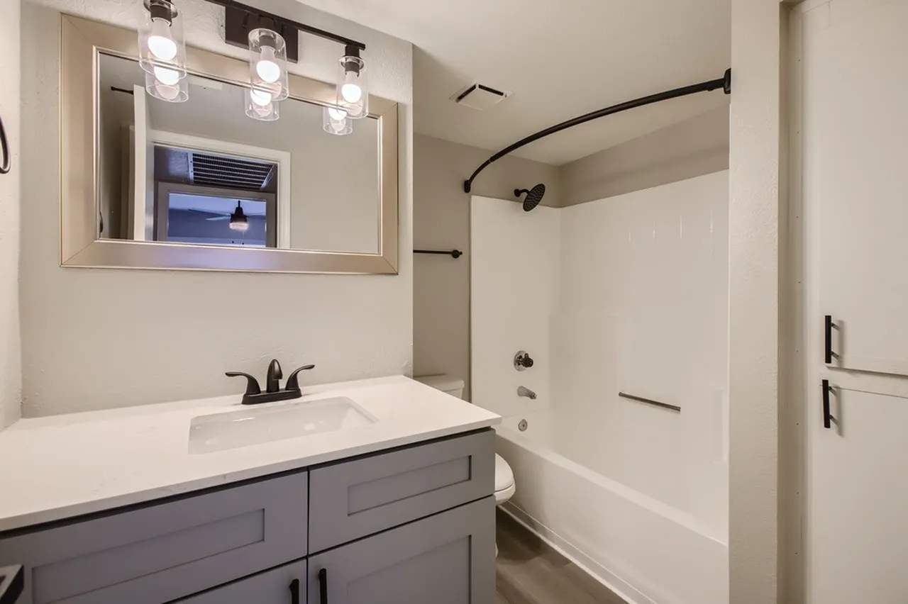 Bathroom, white vanity with gray cabinet, framed mirror, tub shower with curved rod, black shower fixtures