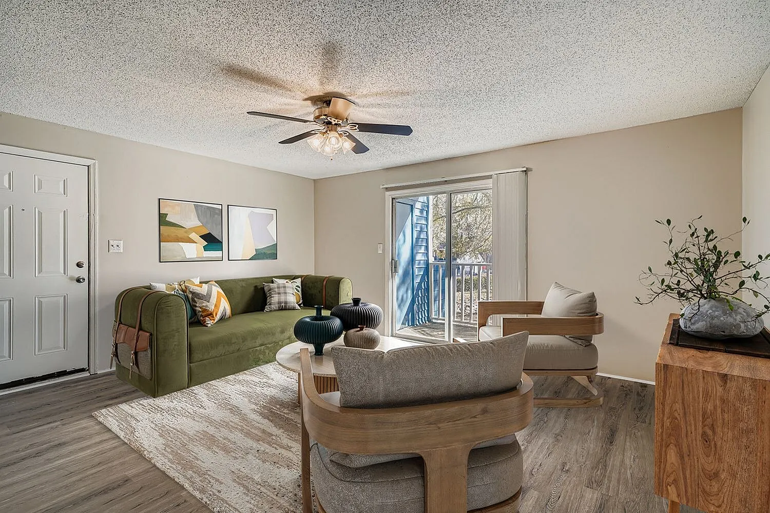 Living room, wood-style plank flooring, ceiling fan, green upholstered sofa, glass patio door