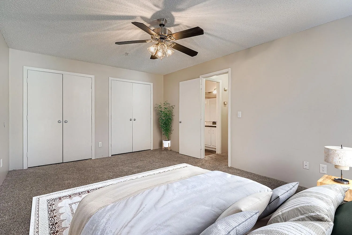 Primary bedroom, carpeted flooring, ceiling fan with light fixture, white closet doors, ensuite bathroom