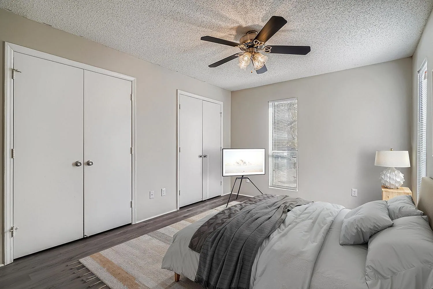 Primary bedroom, wood-style plank flooring, white closet doors, ceiling fan with light fixture