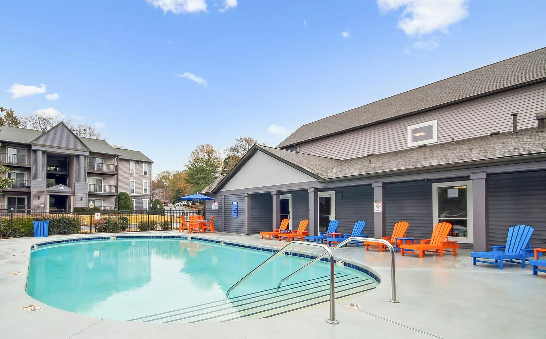 Resort-style pool, lounge chairs, clubhouse, residential buildings, clear sky