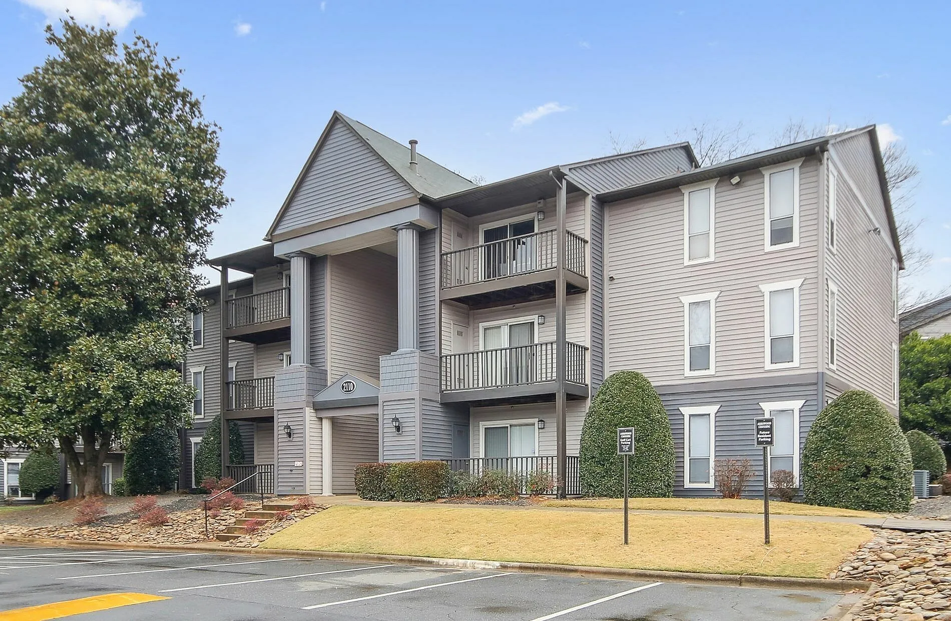 Exterior apartment building, light gray siding, multi-level balconies, manicured landscaping