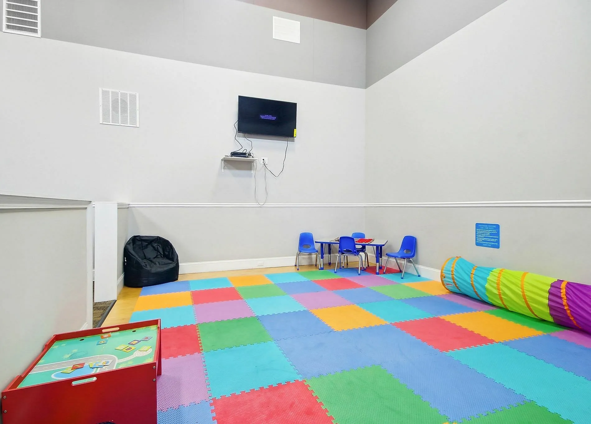 Activity room, colorful foam floor tiles, blue chairs, play tunnel, wall-mounted television