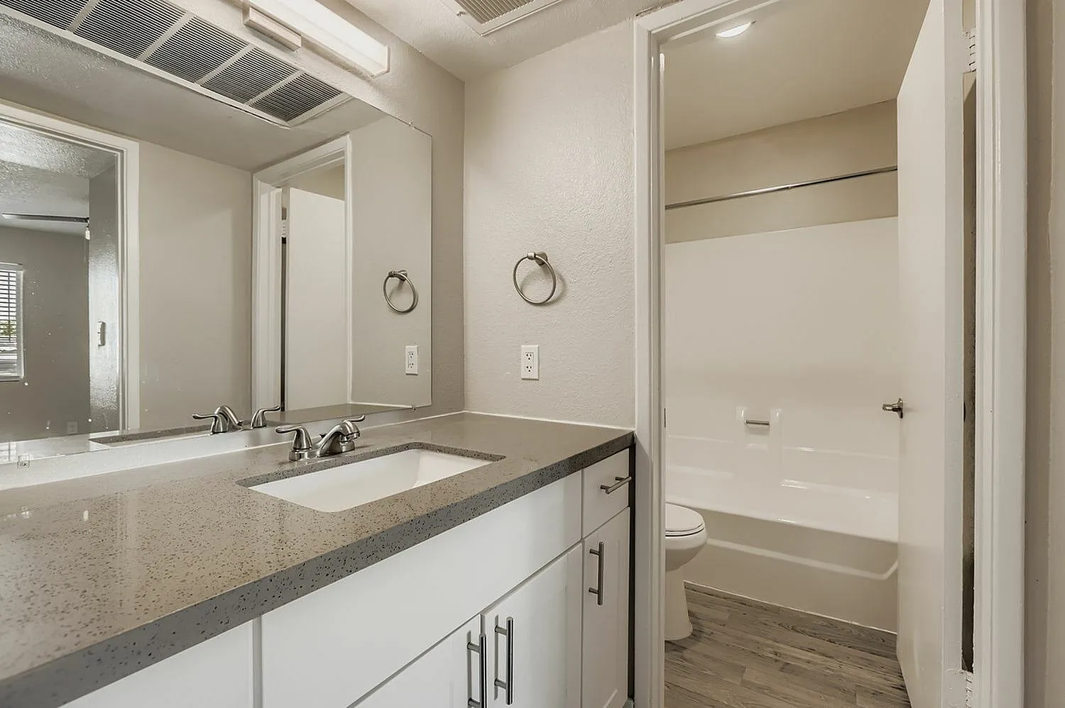 Primary bathroom, gray quartz countertops, white cabinetry, dual sink vanity, wood-style plank flooring
