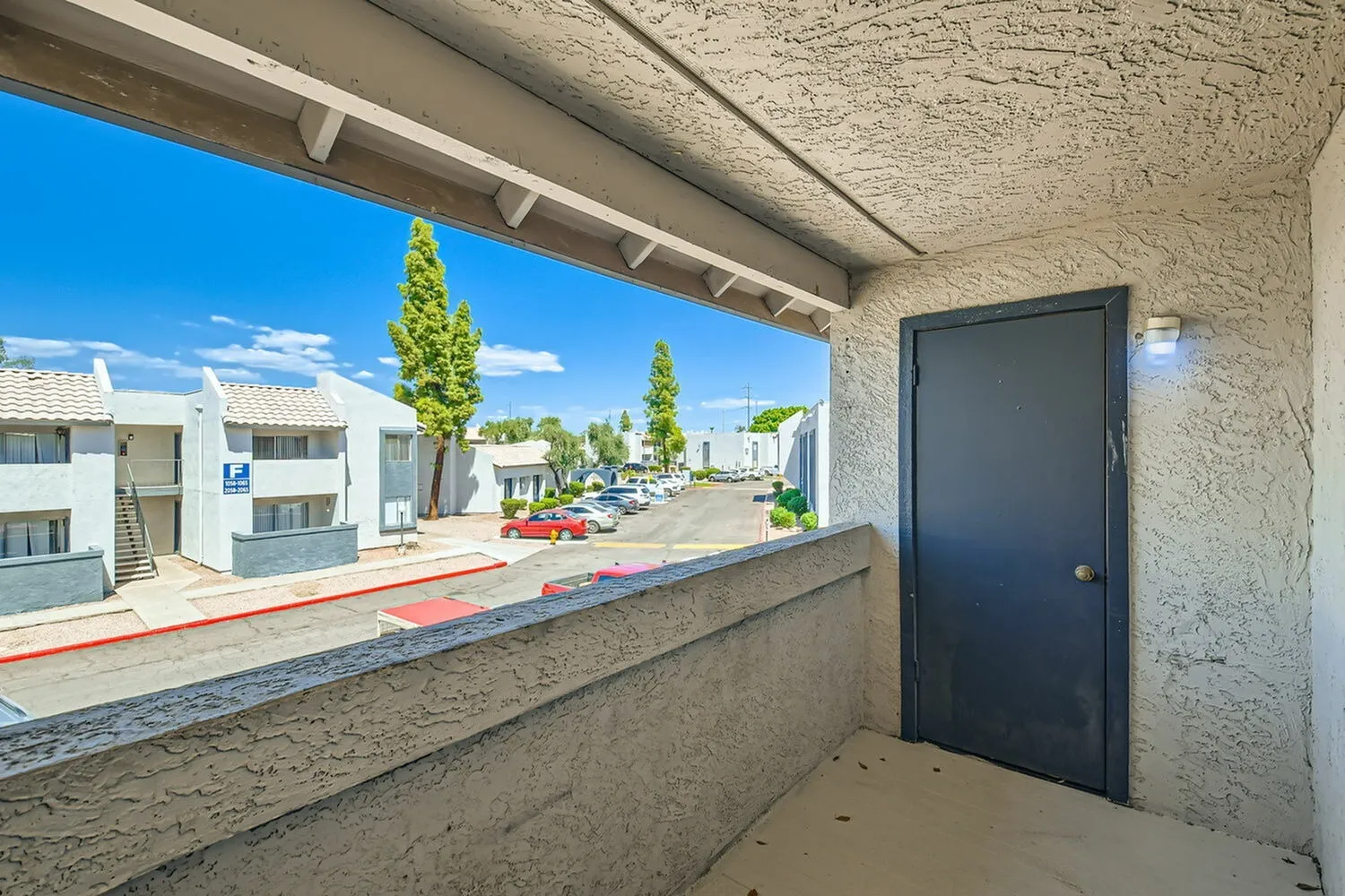Covered patio, concrete flooring, dark entry door, street view with landscaping
