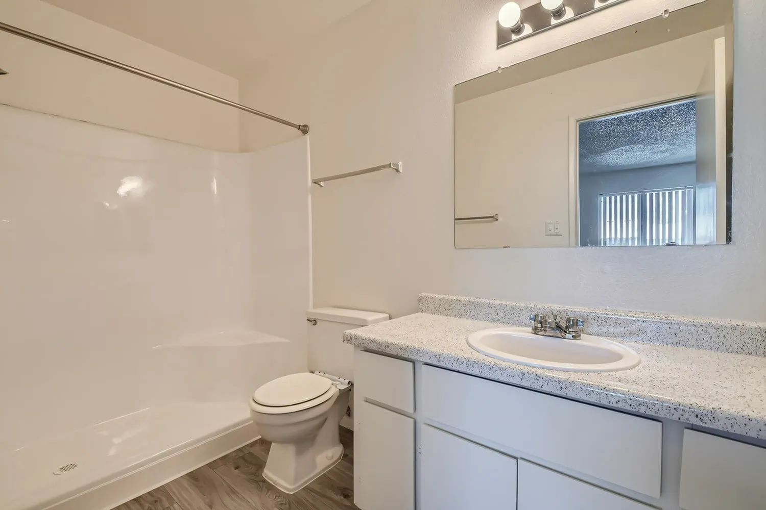 Primary bathroom, white vanity cabinetry, quartz countertops, round sink, mirror, wood-style plank flooring