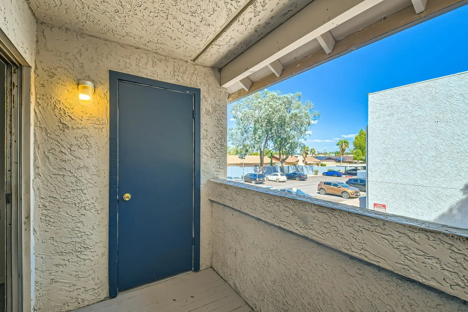 Covered entry, navy blue door, textured stucco walls, yellow sconce, parking lot view