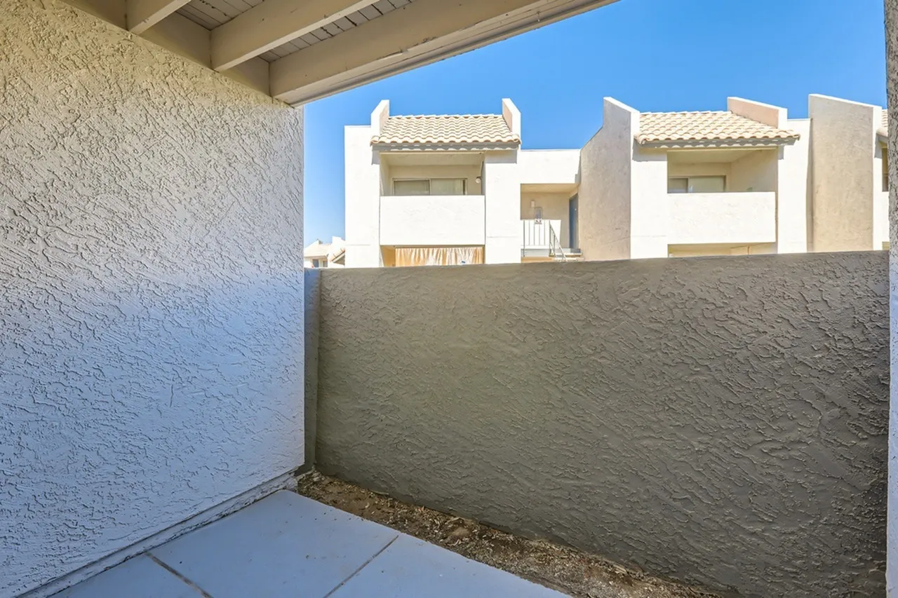 Covered patio with textured stucco walls, concrete flooring, view of neighboring white stucco buildings with tile roofs under clear sky