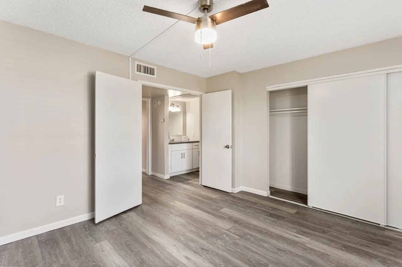 Primary bedroom, wood-style plank flooring, ceiling fan, ensuite bathroom visible