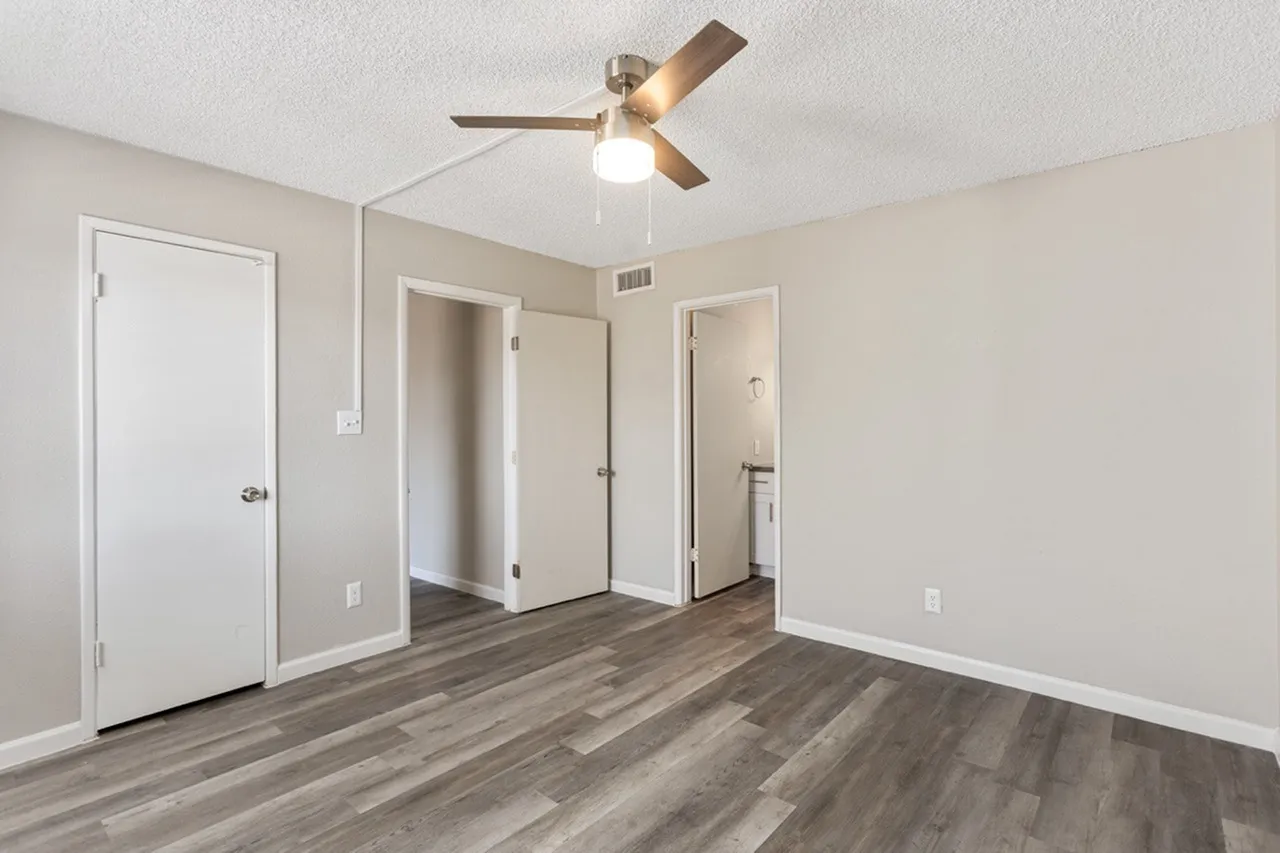 Primary bedroom, wood-style plank flooring, ceiling fan with light, white doors leading to ensuite bathroom