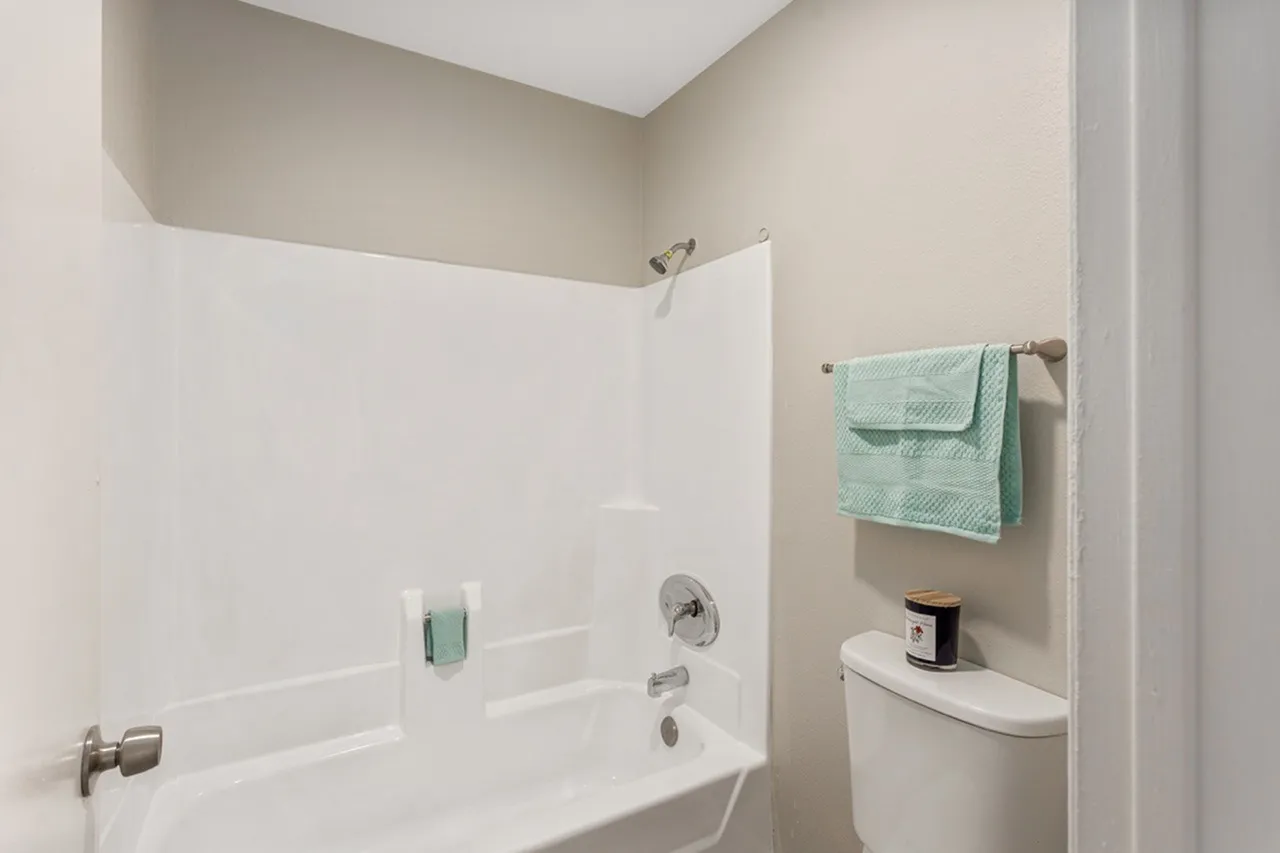 Bathroom, white tile surround, chrome fixtures, mint green towels, white toilet
