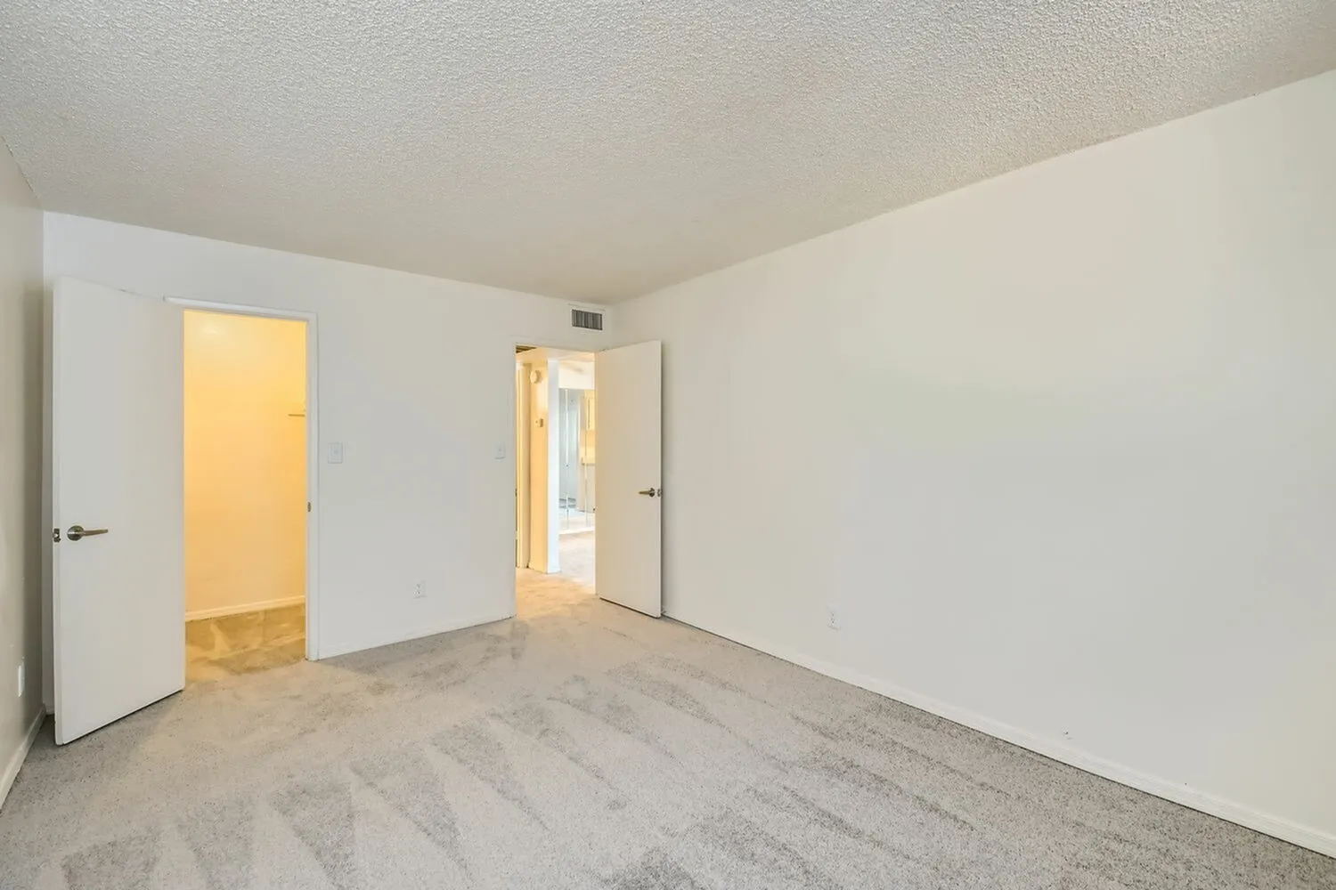 Bedroom, light gray patterned carpet, white walls and ceiling, multiple doorways