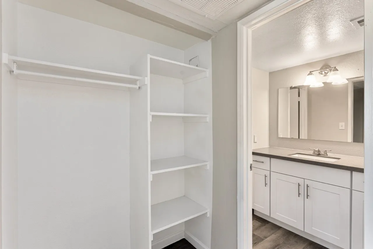 Walk-in closet with shelving and clothing rod, white cabinetry bathroom visible through doorway