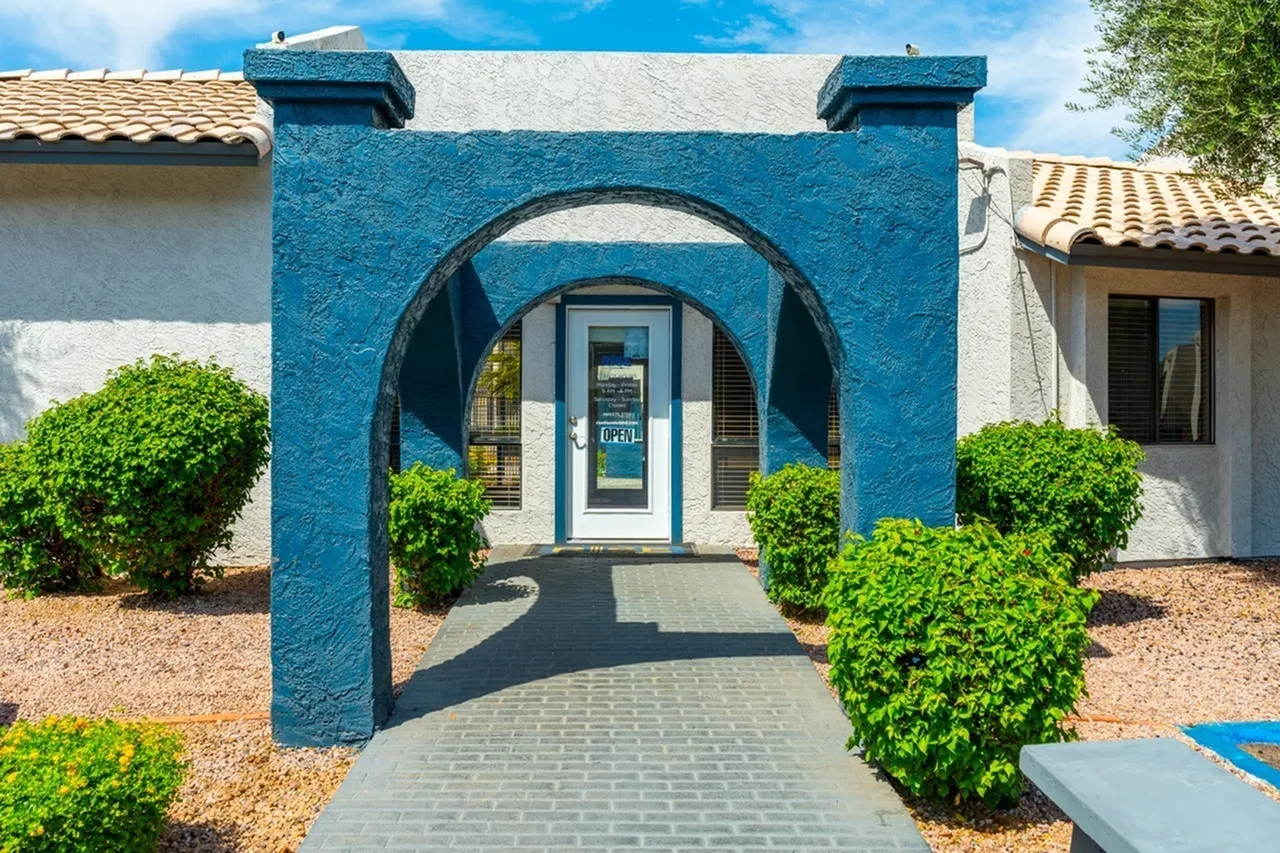 Entry courtyard with blue arch gateway, white door, rounded green shrubs, paver pathway