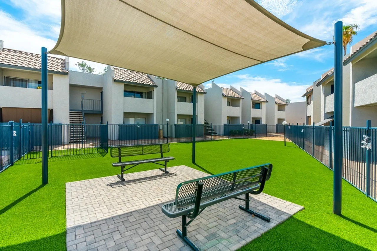 Community courtyard with shade sail, benches, synthetic turf, blue fencing