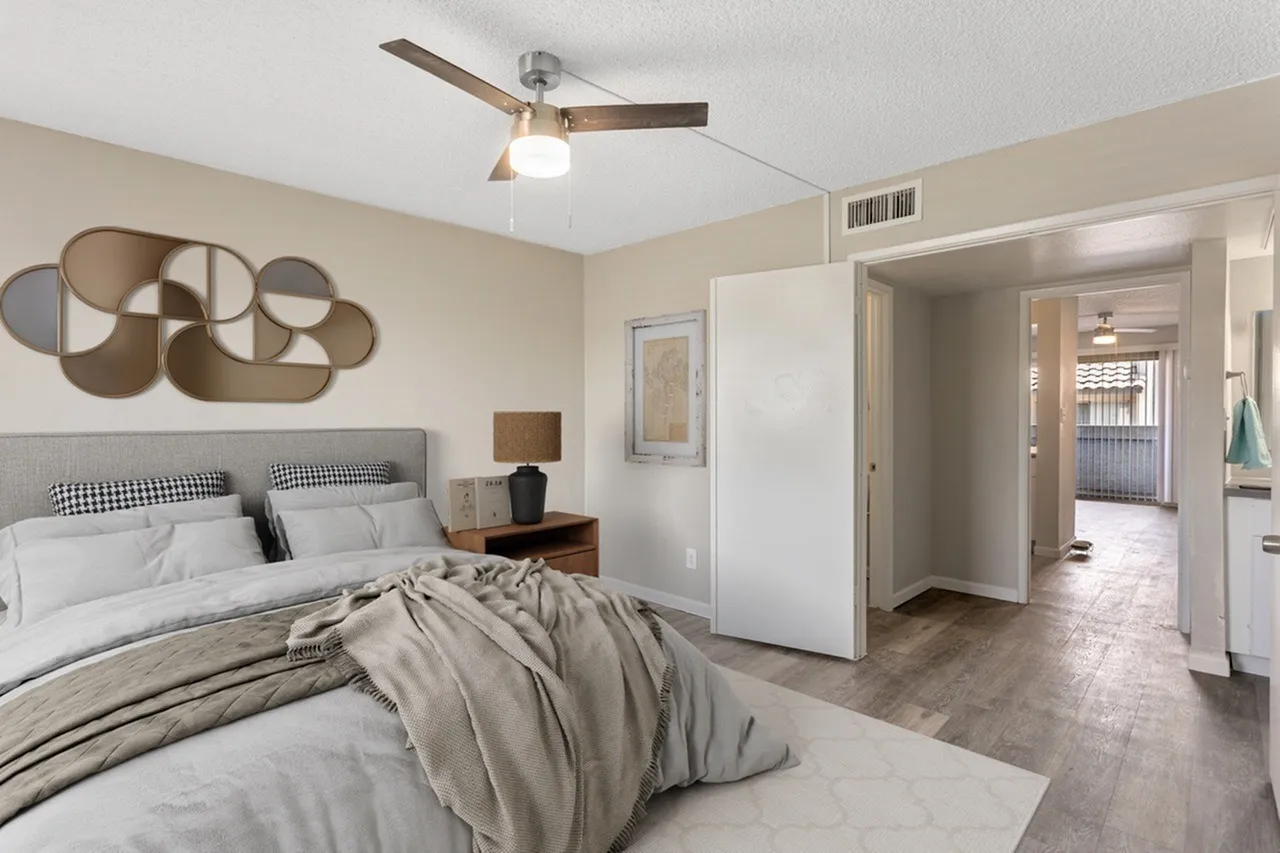 Primary bedroom, wood-style plank flooring, ceiling fan with light, decorative wall art, open ensuite bathroom entry