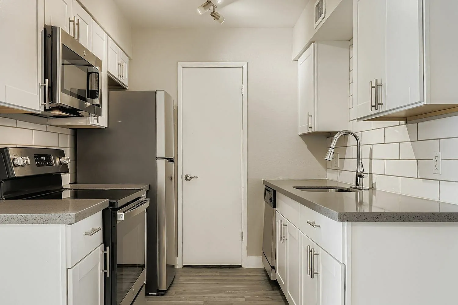 Galley kitchen, white shaker cabinetry, gray quartz countertops, stainless appliances, subway tile backsplash, wood-style plank flooring