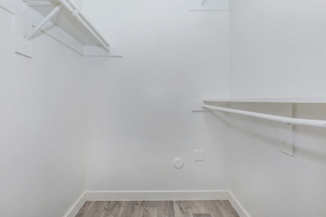 Walk-in closet, white walls, built-in shelving, wood-style plank flooring