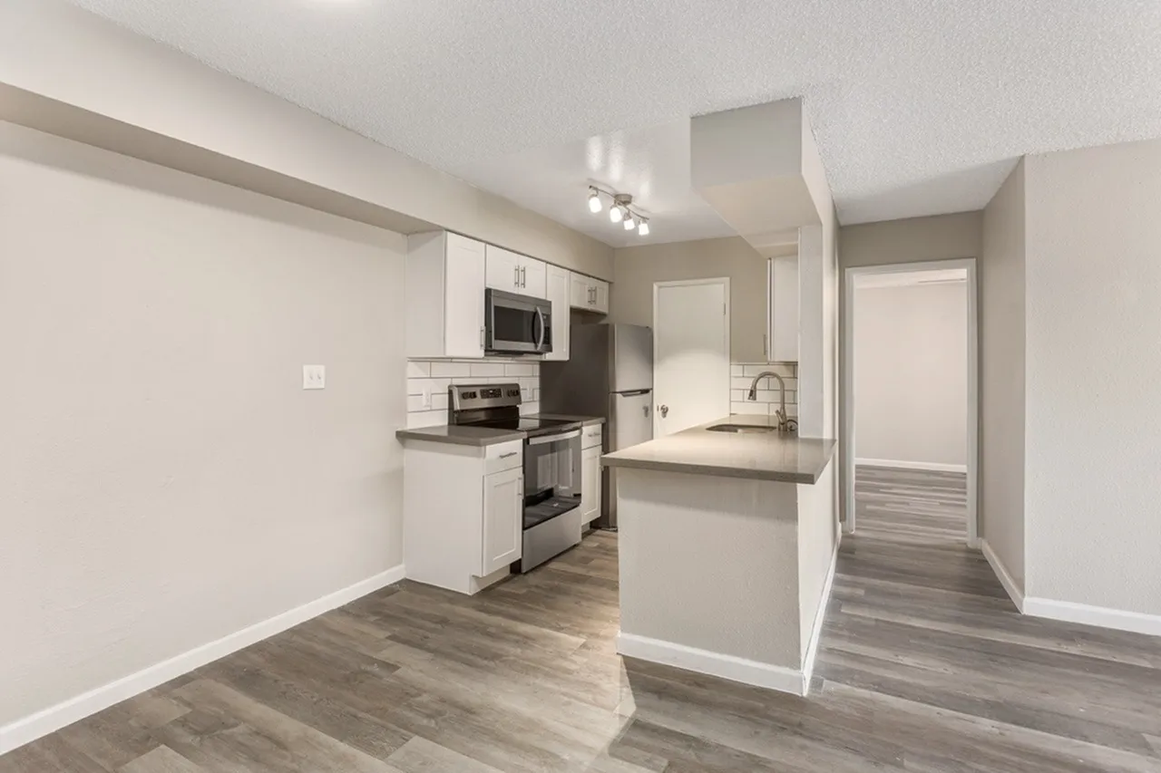 Kitchen with white shaker cabinetry, stainless appliances, gray countertops, wood-style plank flooring, island, pendant lighting