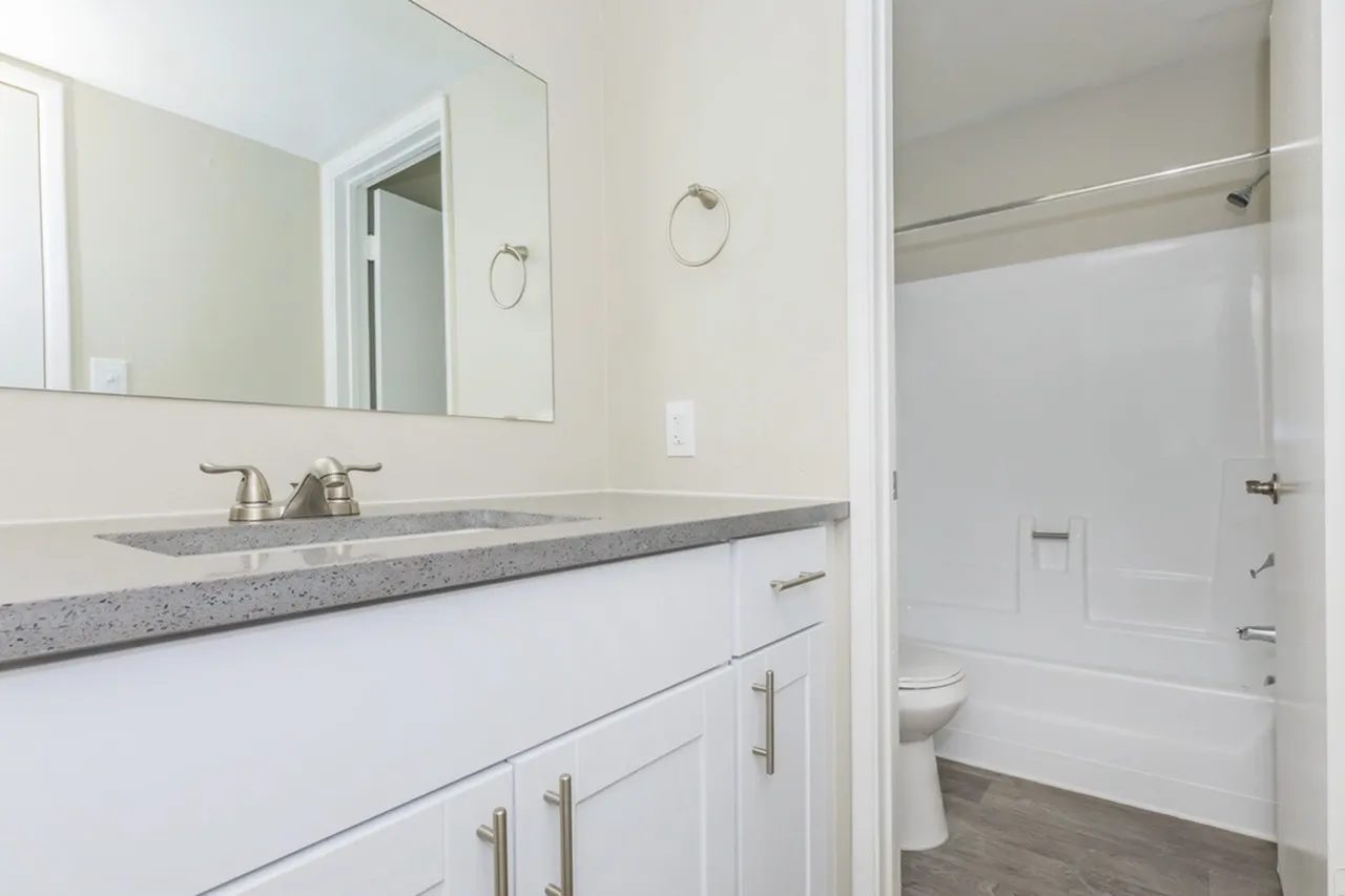 Primary bathroom, white shaker cabinetry, speckled gray countertops, rectangular mirror, tile shower