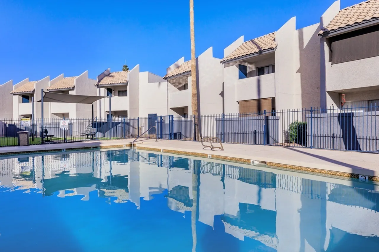 Swimming pool, white townhomes with tile roofs, metal fence, clear blue water