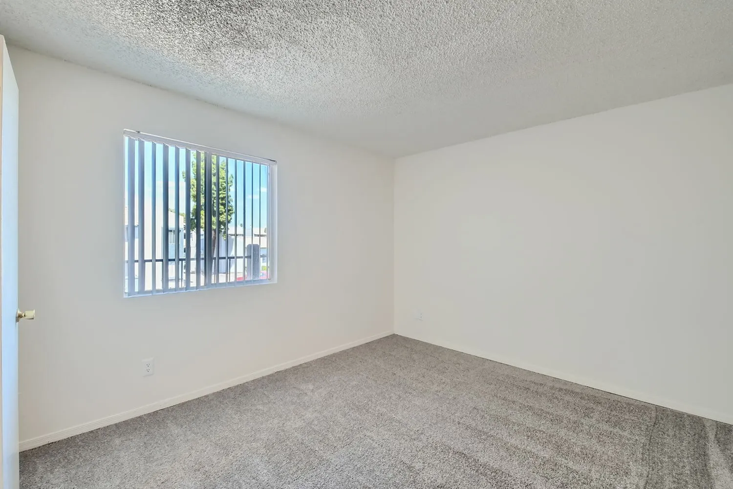 Bedroom, vertical blinds at window, gray carpet flooring, white walls, textured ceiling