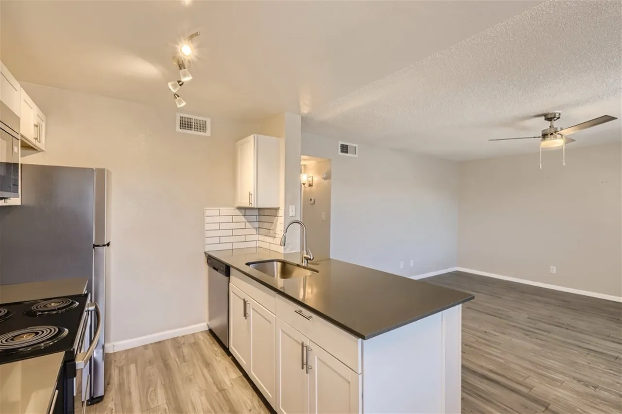 Kitchen, white cabinetry, black countertops, subway tile backsplash, stainless appliances, wood-style plank flooring, open to living room
