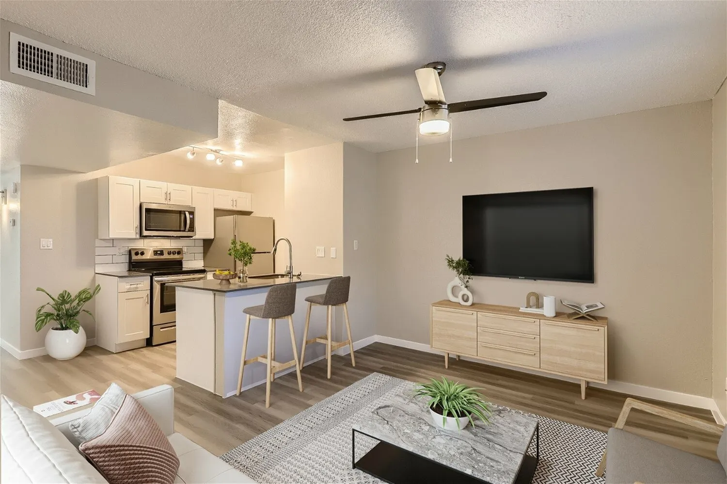 Open concept living and kitchen, wood-style plank flooring, cream cabinetry, stainless appliances, ceiling fan