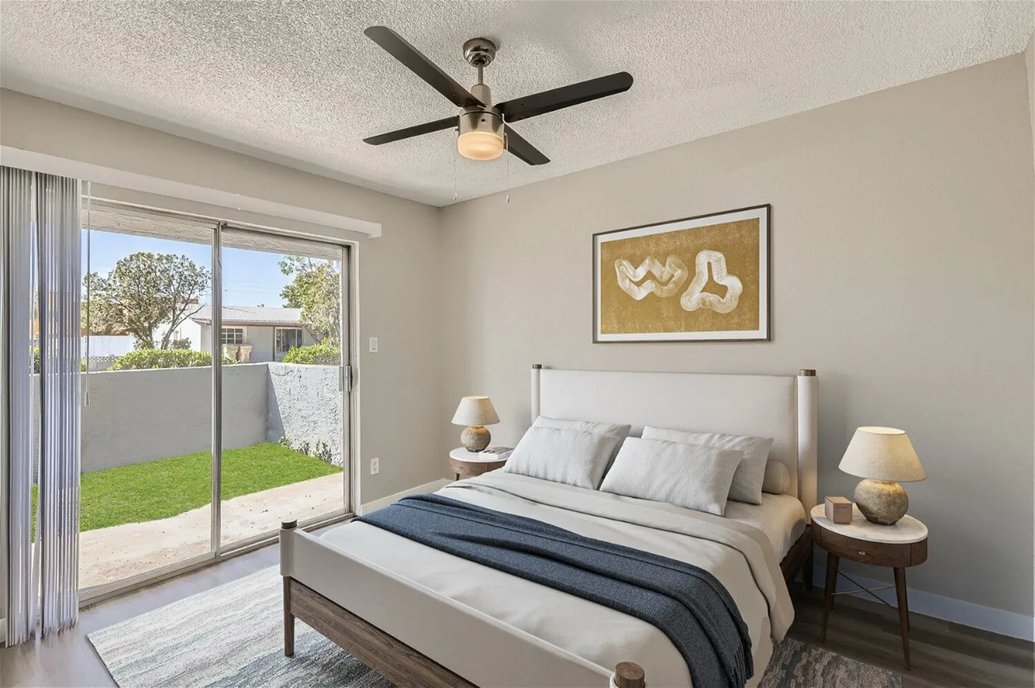 Primary bedroom, upholstered bed frame, wood-style plank flooring, ceiling fan, glass sliding doors to patio