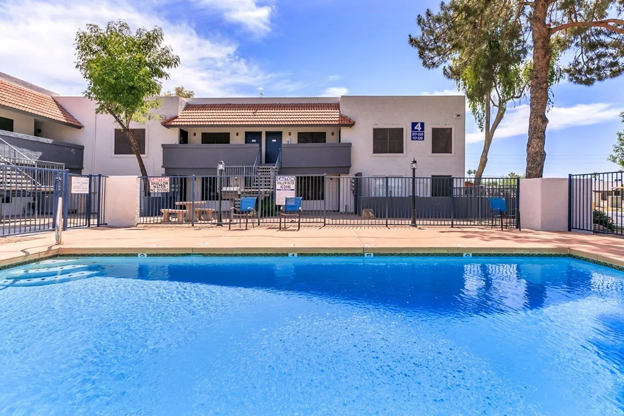 Swimming pool, metal fencing, lounge chairs, landscaping, apartment building