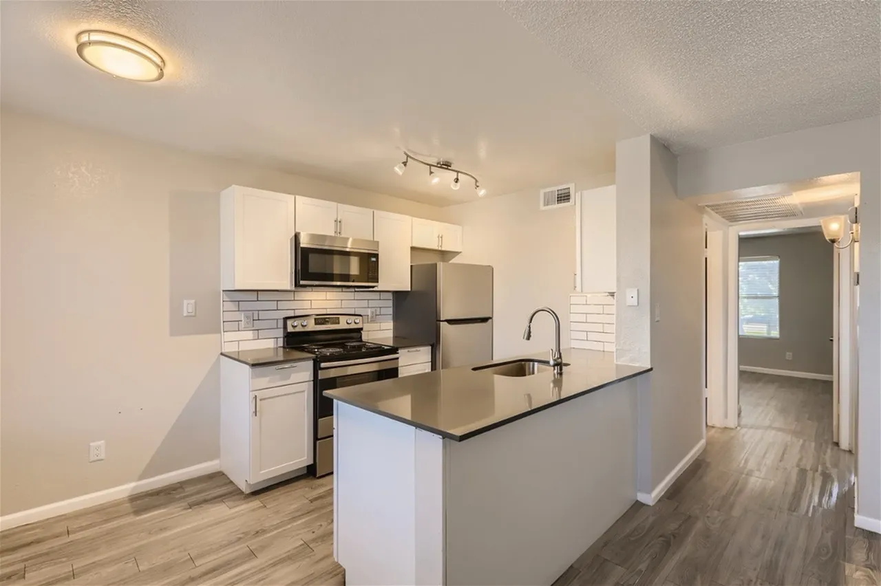 Kitchen, white shaker cabinetry, black quartz countertops, stainless appliances, wood-style plank flooring