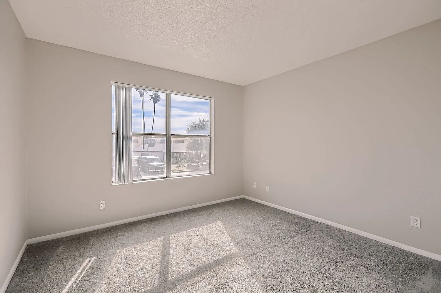 Bedroom, carpet flooring, large window with blinds, neutral walls, natural light