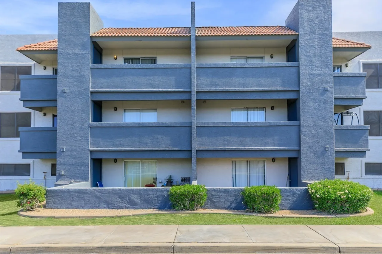 Modern multi-story apartment building, blue and gray facade, balconies, tile roof, landscaping