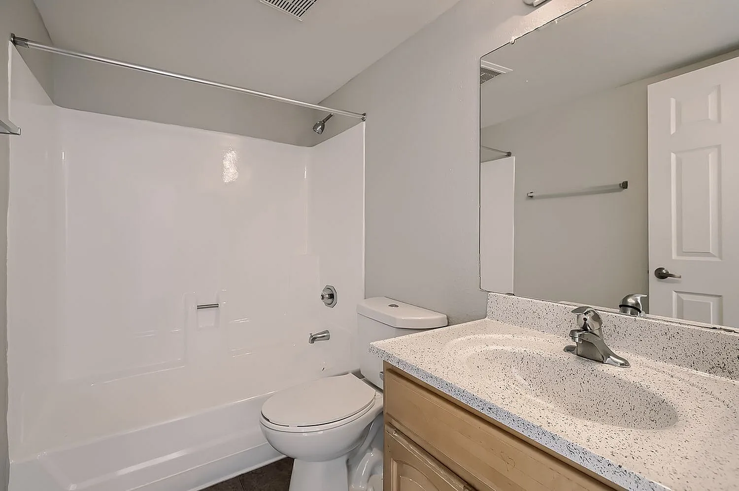 Primary bathroom, light gray quartz countertops, light wood-look vanity cabinetry, large mirror, white subway tile shower surround